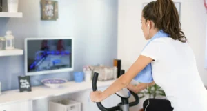 Quale attrezzatura scegliere per l’home fitness. Foto di una donna che si allena a casa su una cyclette